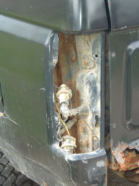 1989 Ford Bronco - The rear tail light housing of a dark green SUV shows significant rust and damage, with wiring and bulb sockets exposed.