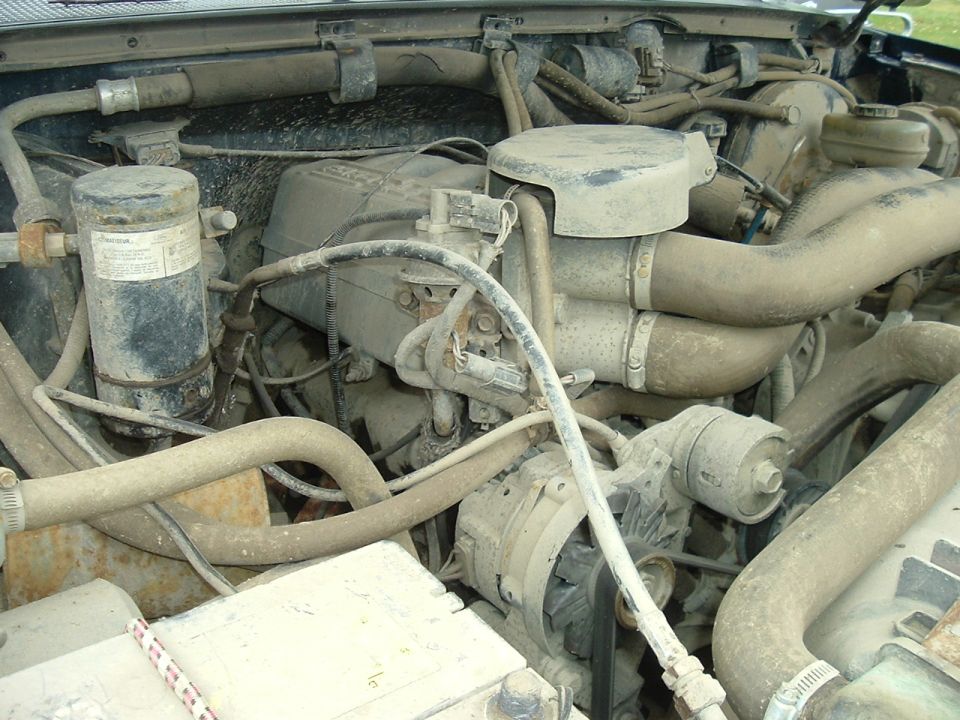 Engine bay with dusty components and hoses, showing alternator and air intake