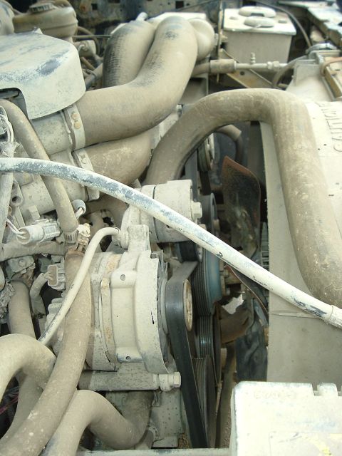 1989 Ford Bronco - Close-up of an engine bay with various hoses, belts, and pulleys visible. Some text is present on a hose.