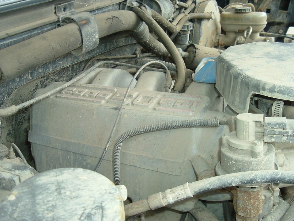 Dusty engine bay with hoses and engine components visible