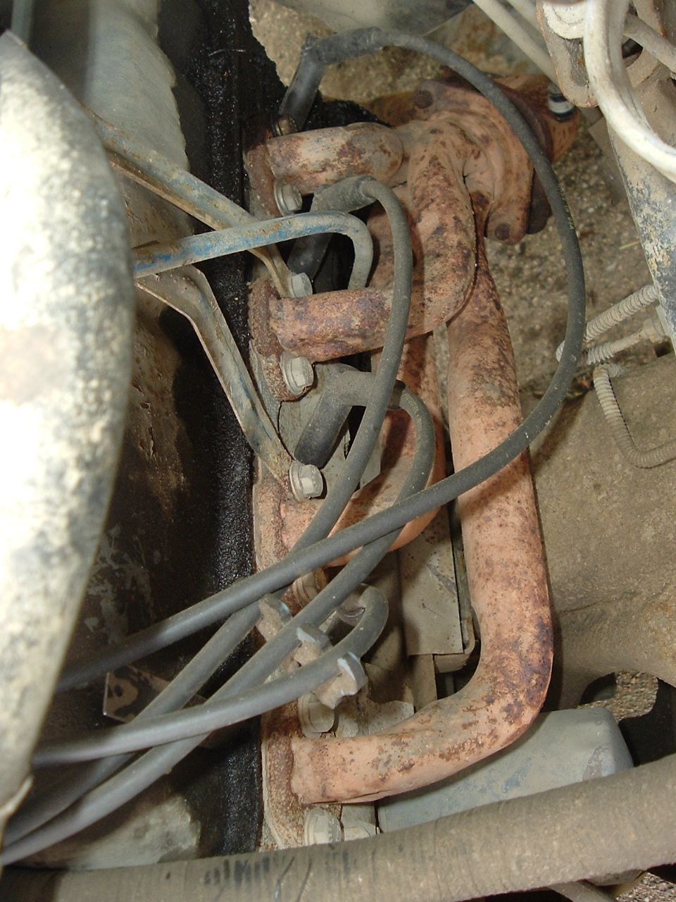 Close-up of a rusty exhaust manifold with spark plug wires attached