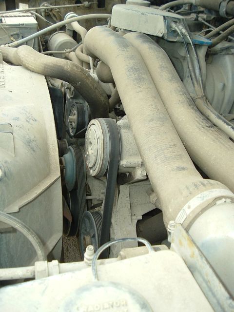 1989 Ford Bronco - Close-up view of a dusty engine bay, focusing on the serpentine belt system and coolant hoses.
