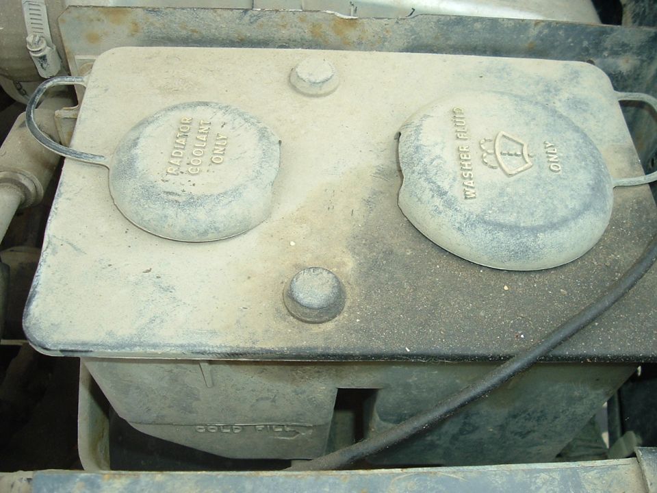 Windshield washer fluid reservoir and radiator coolant cap on dusty engine component