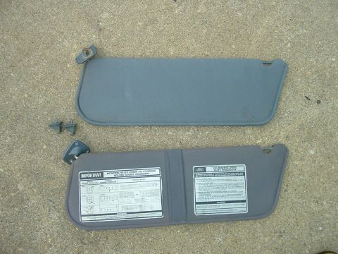 1989 Ford Bronco - Two gray car sun visors with attached mounting hardware and informational stickers are laid out on a concrete surface.