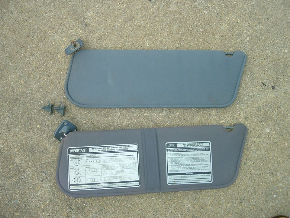 Two gray car sun visors with attached mounting hardware and informational stickers