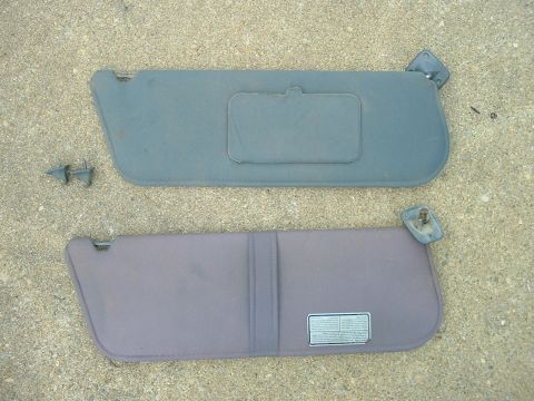 1989 Ford Bronco - Two car sun visors are shown, one gray and one purple, laid out on a concrete surface. The purple visor has a label with text.