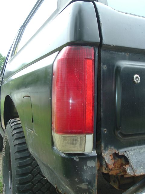 1989 Ford Bronco - The rear corner of a black 1989 Ford Bronco, its taillight and significant rust on the bumper area.