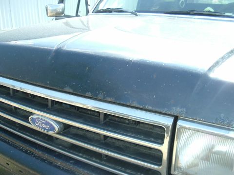 1989 Ford Bronco - Close-up of a dark blue Ford Bronco's front grille and hood, showing the Ford emblem and chrome accents.