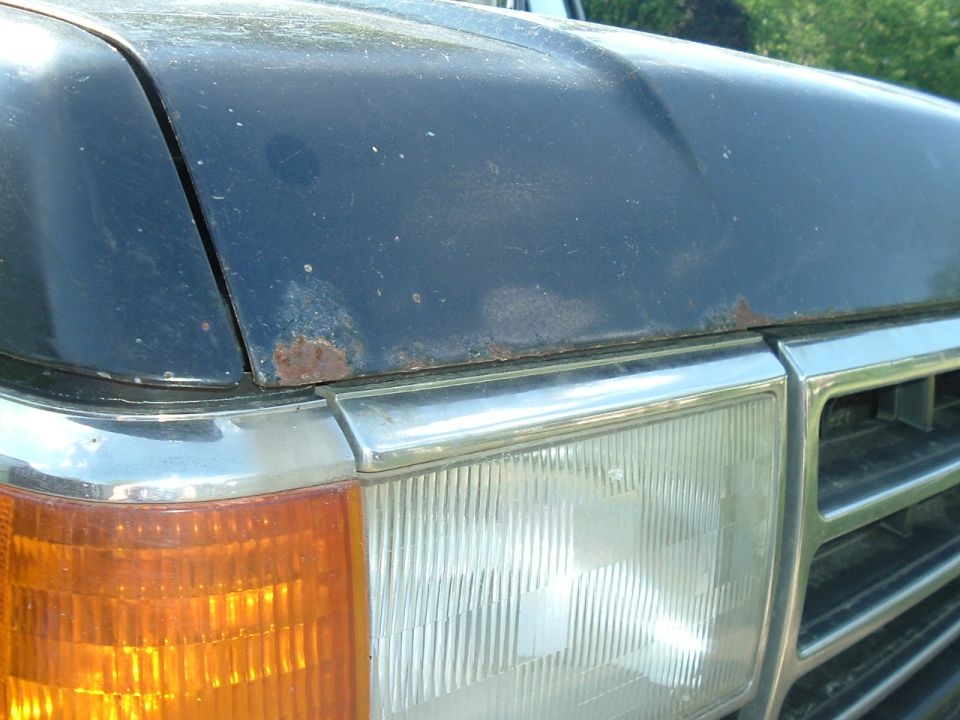 Close-up of 1989 Ford Bronco hood showing rust near the headlight and grille