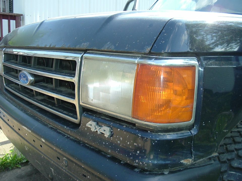 Close-up of a dark Ford truck front clip showing oval grille emblem, headlight and 4x4 badge