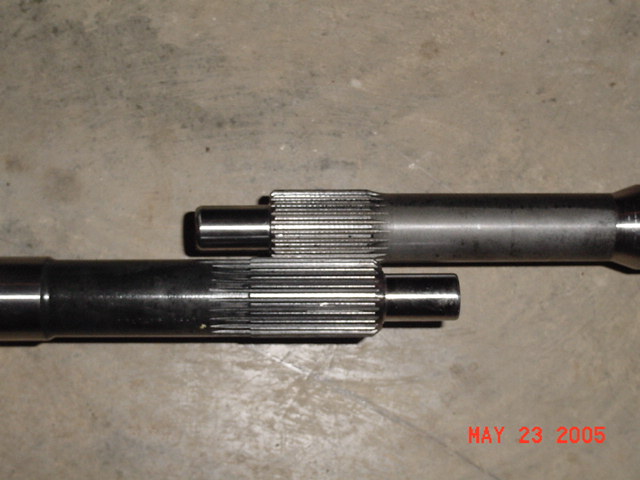 Two splined metal shafts are laid on a concrete surface. One shaft is shorter and appears to be a male end that fits into the longer shaft