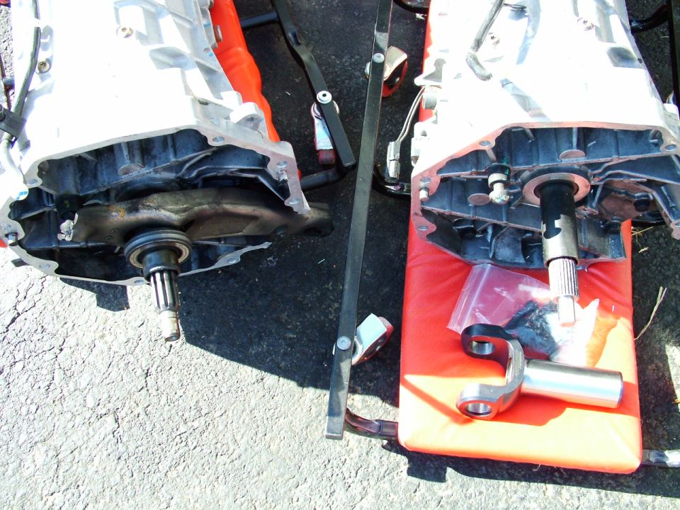 Two disassembled automatic transmissions on a red cushion and asphalt