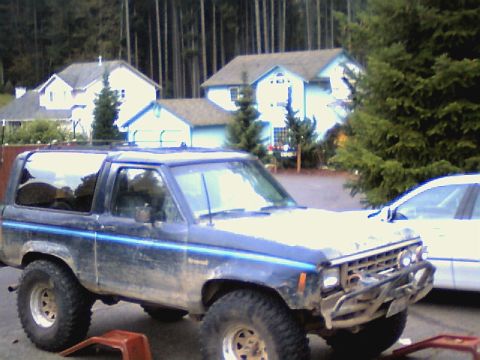 1987 Ford Bronco II - A lifted blue Ford Bronco II sits in a driveway with houses and trees in the background.
