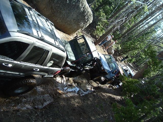 Rotated photo of SUVs on a steep rocky off-road trail with a vehicle tipped against a boulder