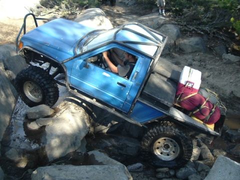 1989 Ford Bronco - This heavily modified pickup truck is shown navigating a challenging rocky trail, loaded with gear in the bed.