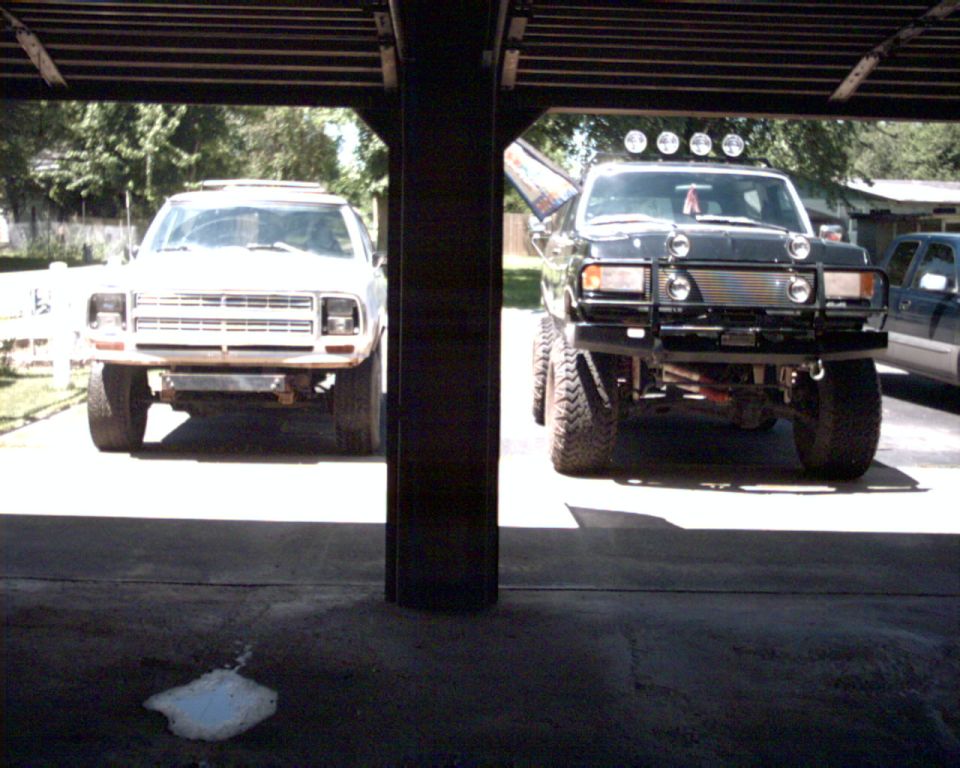 Two lifted square-body Dodge 4x4 trucks head-on in driveway seen from garage