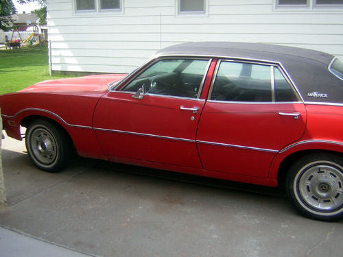 Red four-door sedan with black vinyl roof, side view on driveway