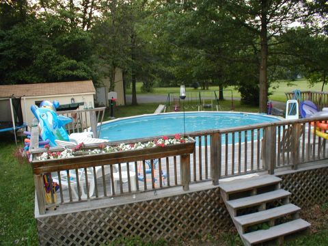 1979 Ford Bronco - A backyard scene an above-ground pool surrounded by a wooden deck and lush green trees.