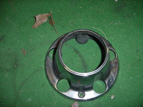 1989 Ford Bronco - A single chrome wheel cover rests on a green surface with a few fallen leaves.