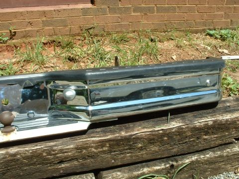 1985 Ford Bronco - A chrome bumper with a black rubber trim and a reflective strip is shown resting on wooden beams.