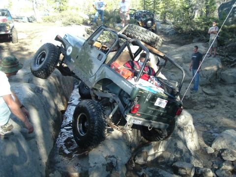 1989 Ford Bronco - A Jeep Wrangler tackles a challenging off-road obstacle, demonstrating its articulation over large rocks.