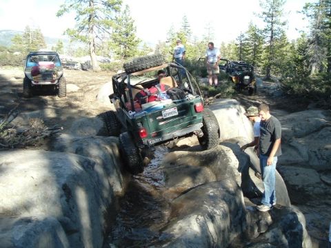 1989 Ford Bronco - Several off-road vehicles traverse a challenging rocky trail in a wooded area.