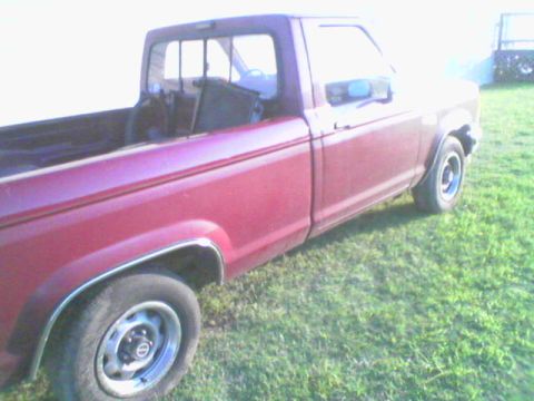 1990 Ford Ranger - A red 1990 Ford Ranger pickup truck is shown from the side, parked on a grassy area.