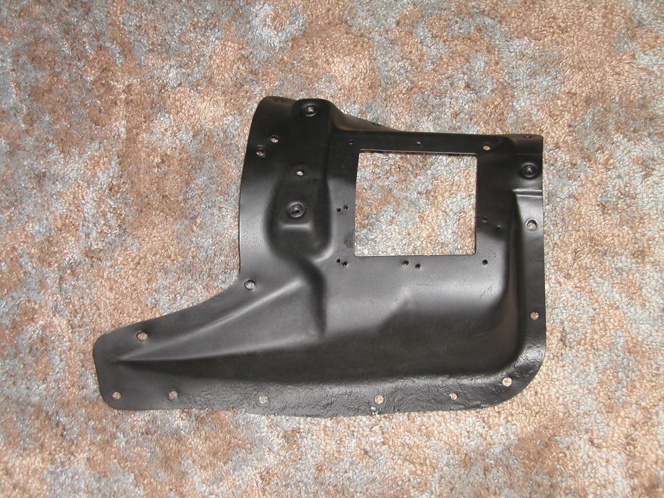 Removed black stamped sheet metal panel with rectangular cutout lying on carpet