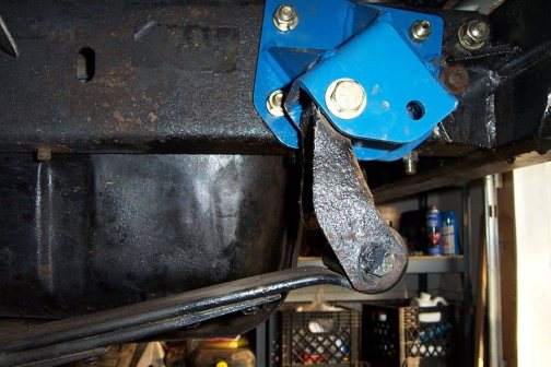 Blue bracket bolted to frame rail with rusty suspension arm underneath, shop background
