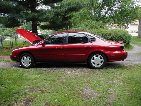 1997 Ford Taurus - A red 1997 Ford Taurus sedan is parked on a grassy area with its hood open, showing a side profile.