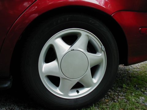 1997 Ford Taurus - Close-up of a red car's rear wheel and tire, a silver hubcap with a five-spoke design.