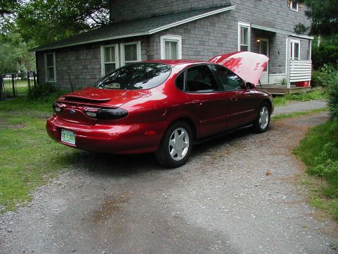 1997 Ford Taurus - A red 1997 Ford Taurus sedan is parked in a gravel driveway, with its hood open, next to a house.