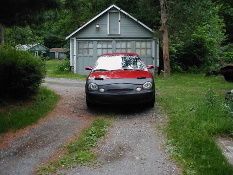 1997 Ford Taurus - This red car with a black car bra is parked in front of a detached garage.
