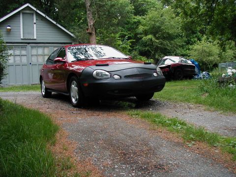 1997 Ford Taurus - Red 1997 Ford Taurus is parked in front of a garage, with another vehicle visible in the background.