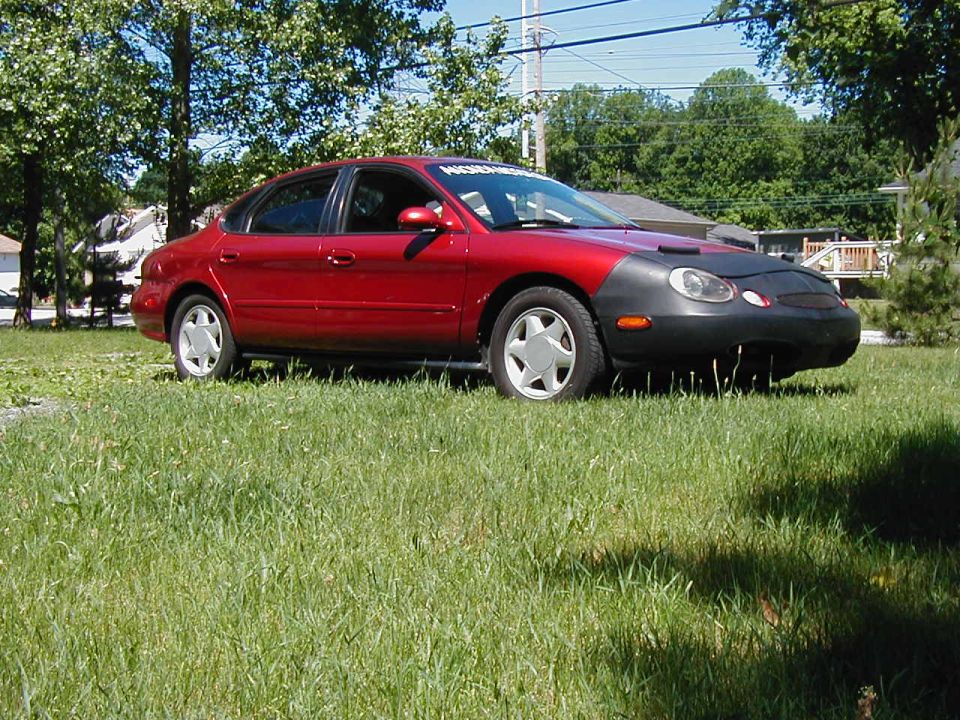 1997 Ford Taurus sedan parked on grass, front end covered by a black car bra