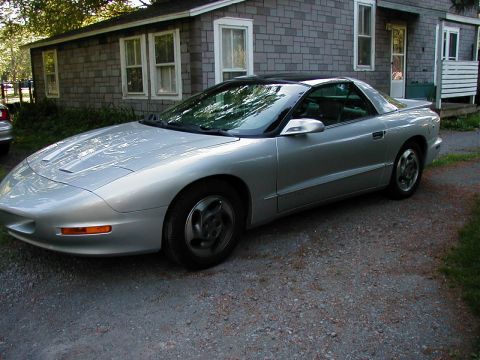 1997 Ford Taurus - A silver 1997 Pontiac Firebird is parked in front of a gray shingled house.