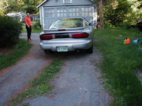 1997 Ford Taurus - A man stands near a silver Pontiac Firebird parked in front of a garage.