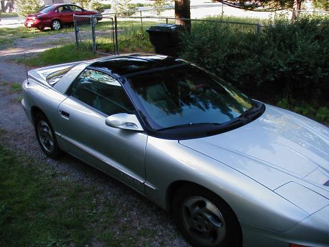 1997 Ford Taurus - A silver Pontiac Firebird is parked in a driveway, with a red sedan visible behind a fence.