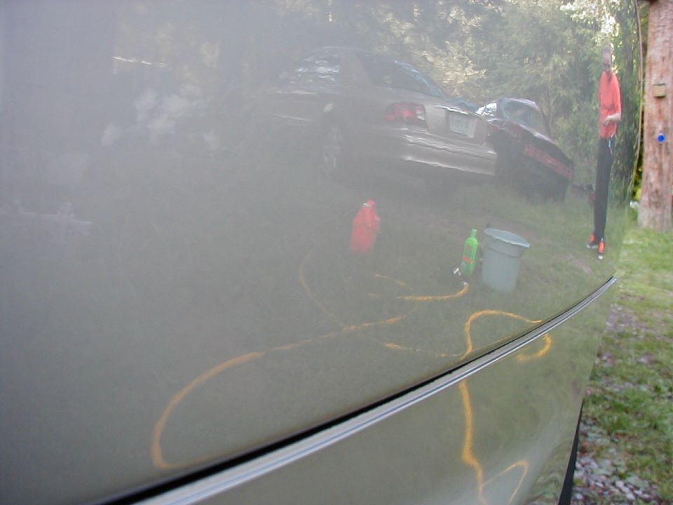 Reflection of a 1997 Ford Taurus being washed, with a hose and bucket visible