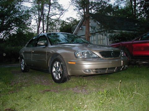 1997 Ford Taurus - Gold sedan parked on grass with a red car and house visible in the background.