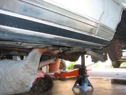 1985 Ford Crown Victoria LTD - A mechanic works on the underside of a car, which is raised on jack stands.