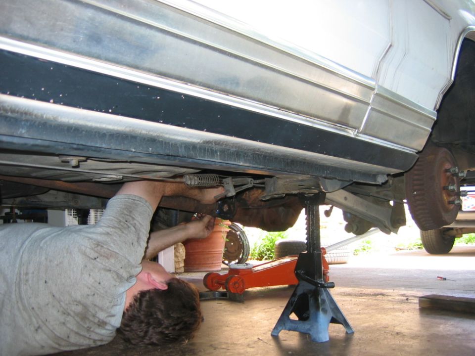 Car undercarriage with a person working on the suspension, supported by jack stands
