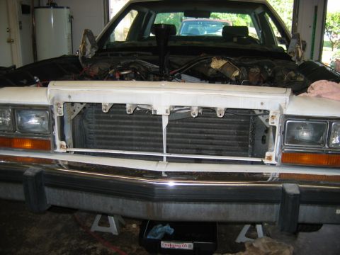 1985 Ford Crown Victoria LTD - The front of a car is shown with the hood up, revealing the engine bay and radiator, as it sits on jack stands.