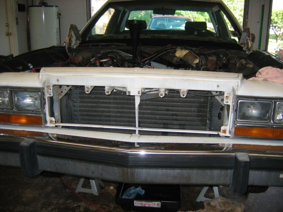 car front end with hood open, radiator exposed, engine bay visible, car on jack stands