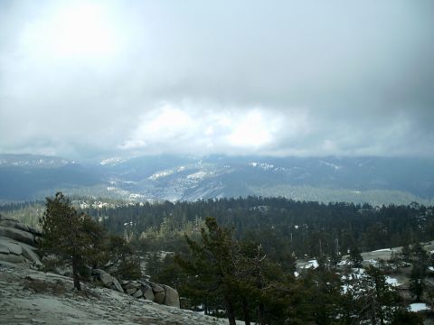 1989 Ford Bronco - Overcast sky above a vast mountain range covered in pine trees and scattered snow.