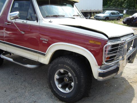 1986 Ford Bronco - The front end of a red and white Ford Bronco shows damage to the hood and grille area.