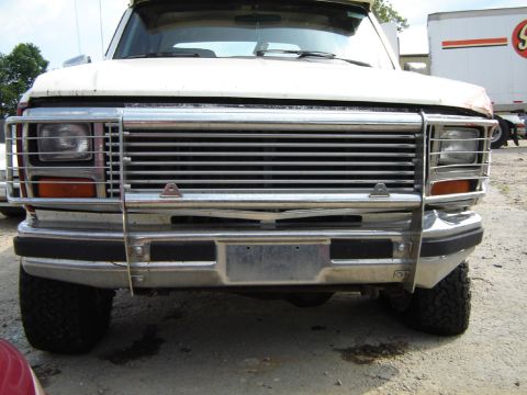 1986 Ford Bronco - Front view of a white Ford Bronco with a chrome grille guard, showing a damaged grille.