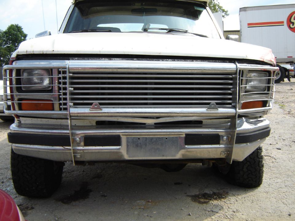 White Ford Bronco with chrome grille guard, front view. Damaged grille