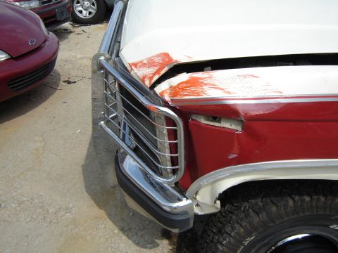 1986 Ford Bronco - The front end of a 1986 Ford Bronco shows significant damage to the hood and fender, with a chrome grille guard still intact.