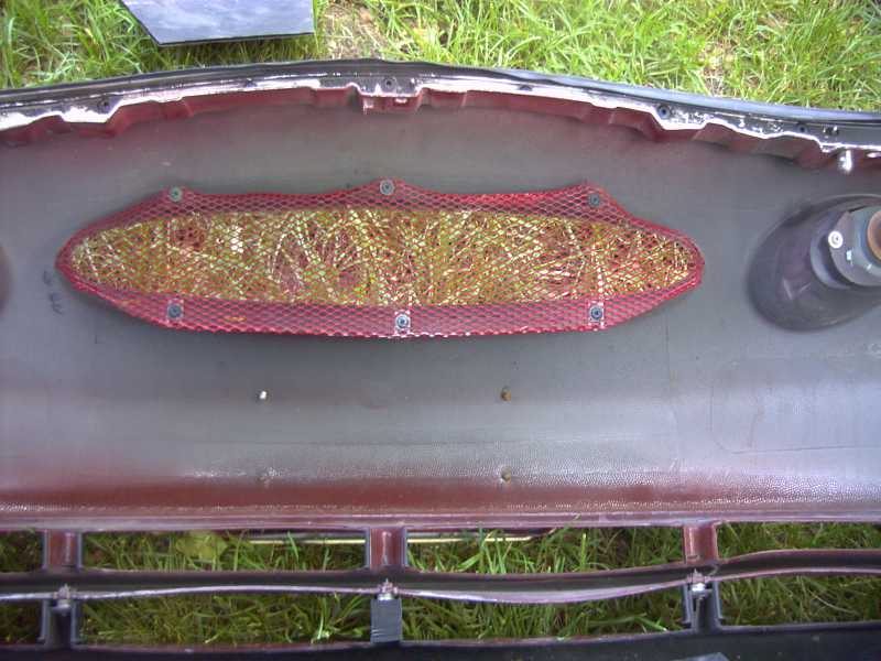Inside of a car bumper with red mesh covering an opening